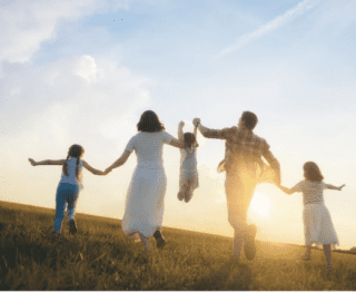Family walking in field lifting child with sunsetting